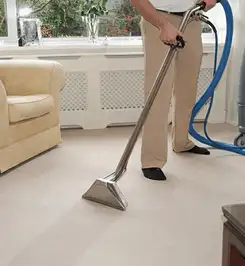 Professional carpet cleaner using a hot-water extraction wand and hose machine in a living room in Ogden, UT.