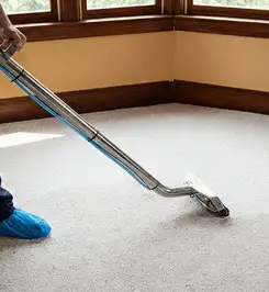 Steam carpet cleaning technician using a hot-water extraction wand on a residential carpet, wearing blue protective shoe covers Ogden, UT.