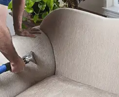 Professional upholstery cleaner deep-cleaning a fabric sofa with a handheld extraction tool and hose in Ogden, UT.
